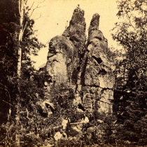 Monument Rock, 65 feet high, in the woods on Isle Royal, Lake Superior. (Note the people standing on the top at the base.) Folder 7, Box 1, UM Scientific Expedition to Lake Superior.