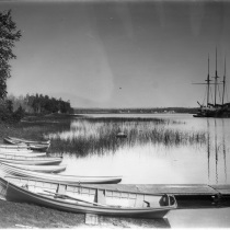 Les Cheneaux, Michigan. Canoes in water along beach (lined in a row). Island properties and sailing ship in the distance. Box 14, Andrew Tanner Photographs