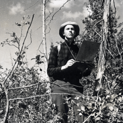 University of Michigan student outdoors taking notes on a notepad in a forest.