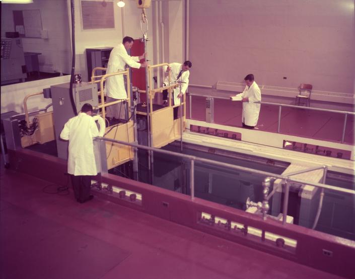 Lab techs in white coats around nuclear machinery. 