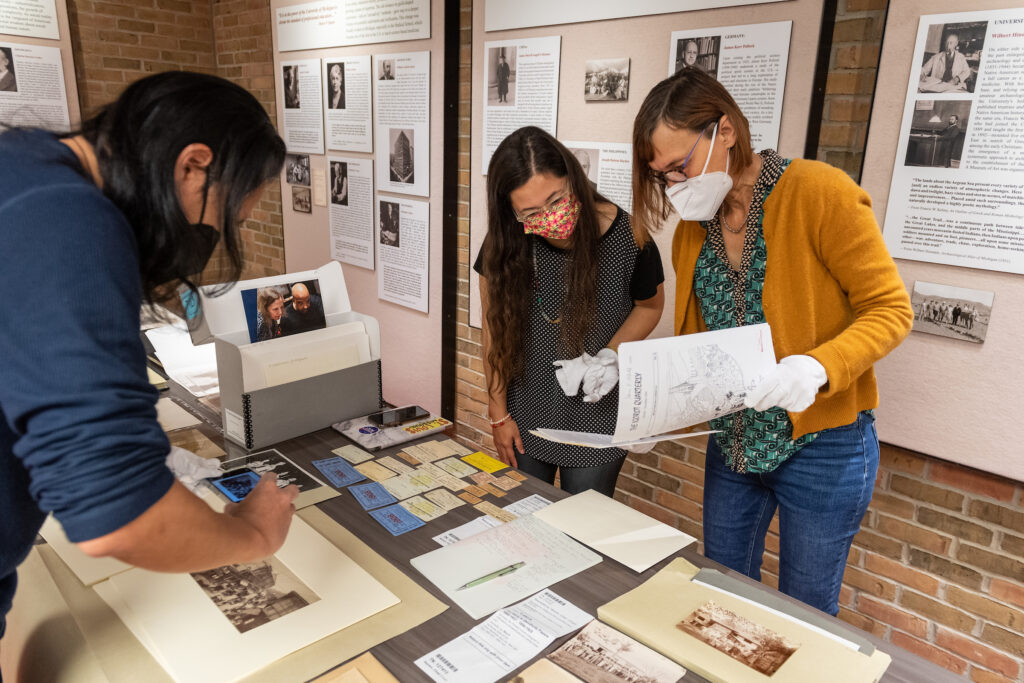 Three students looking at papers and photographs on a table