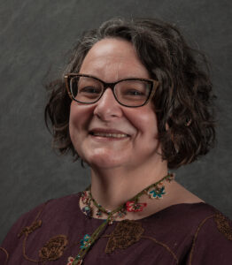 Alexis Antracoli smiles and wears glasses in this portrait photograph. 
