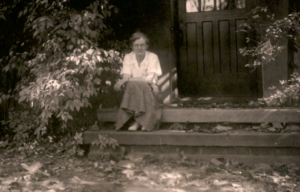 Black and white photo of Helen Thompson Gaige sitting on steps wearing white shirt and skirt. 