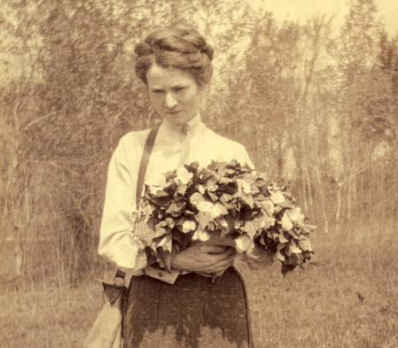 Helen Thompson Gaige walking outdoors, holding an arm-full of ivy. 