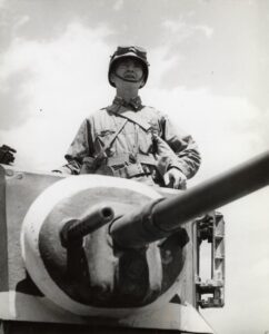 Frank Murphy standing in a tank dressed in Army fatigues. 