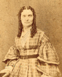 Sepia-toned photo showing a woman in a checkered dress with shoulder-length brown hair.
