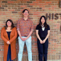Three students standing against a brick wall.