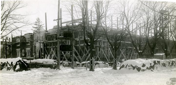 Black and white photo showing wooden scaffolding around a building being constructed.