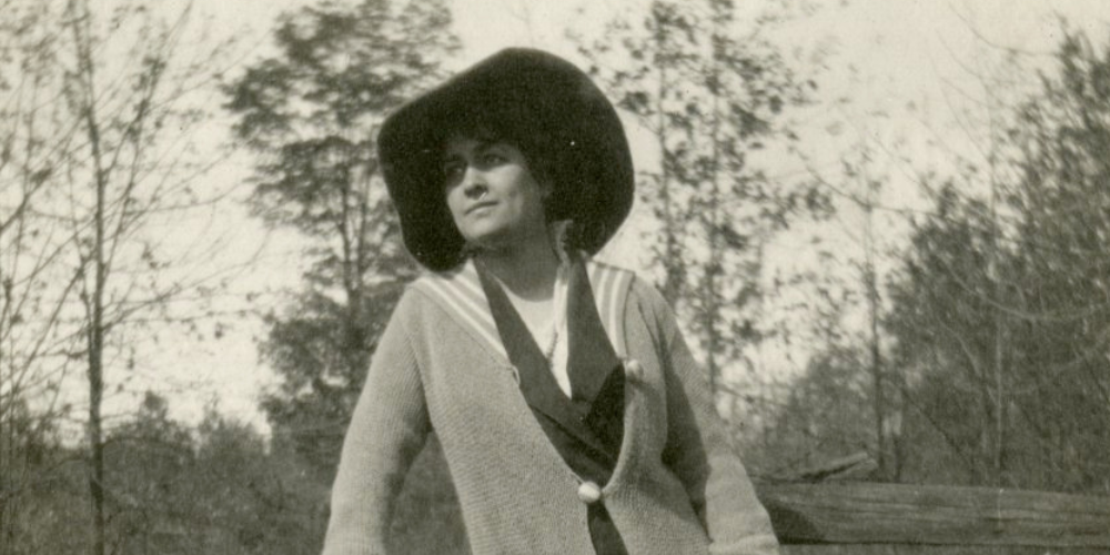 Poet Angela Morgan wearing a hat and sweater in a field with trees.