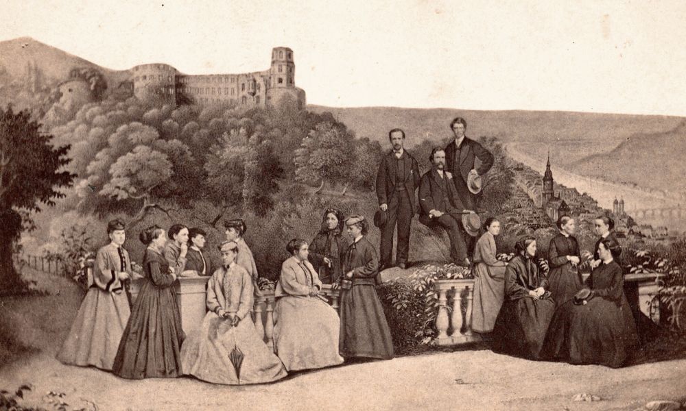 Lucinda Stone with a group of women students in Heidelberg, Germany, posed in front of a background showing trees and a large stone building, along with three men, who are likely her husband and sons.