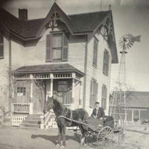 A man with a horse and buggy in front of a farmhouse.