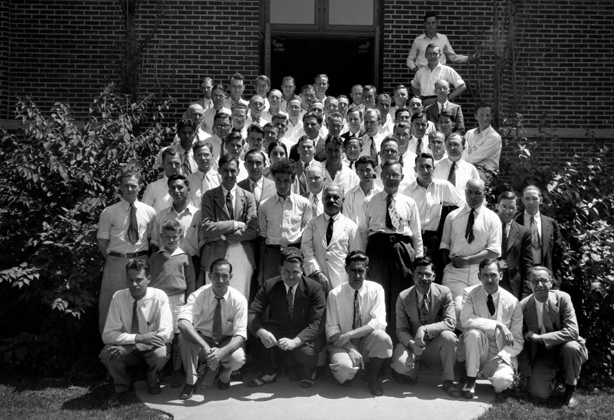 A group of people attending UM physics symposium pose for photo on the steps of a brick building, Summer 1931 in Ann Arbor.