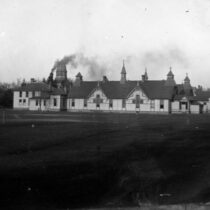 The University of Michigan's Homeopathic Medical School circa 1890-1910, a series of connected buildings with several chimneys set on a grassy lawn.