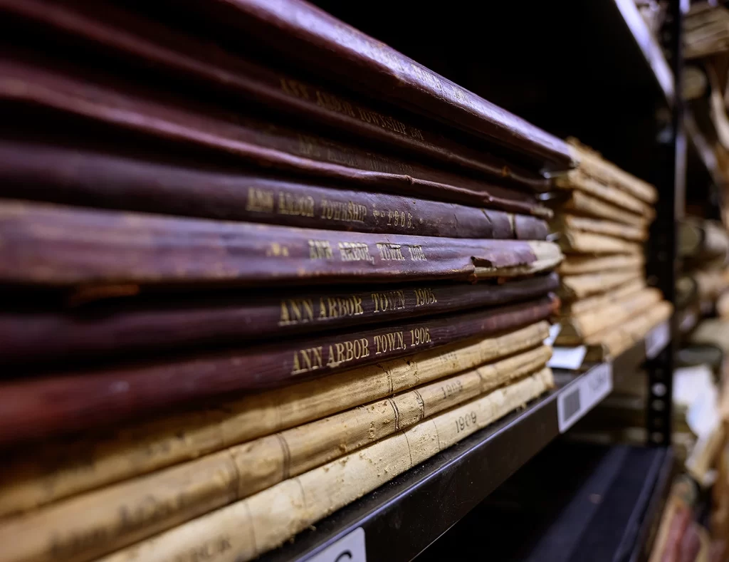 A side view of a bookcase inside the Bentley Historical Library's archives, featuring a stack of large books with spines labeled "Ann Arbor Town" from the 1900s.