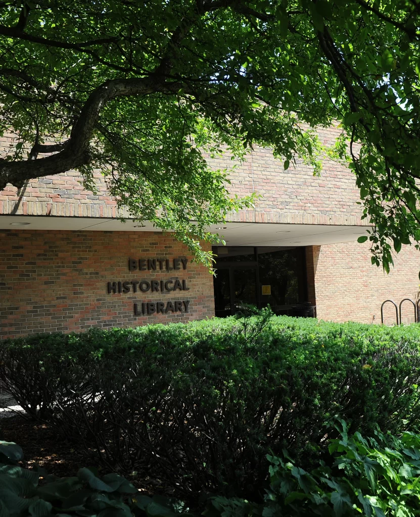 The brick front entrance to the Bentley Historical Library showing the name of the building, and surrounded by green trees and bushes.