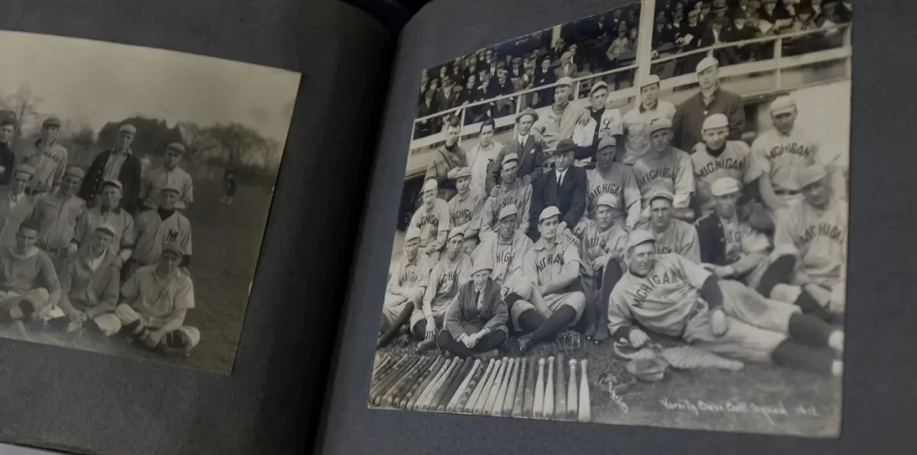A historic scrapbook is open with old, black-and-white baseball photos on both the left and right sides of the spine.