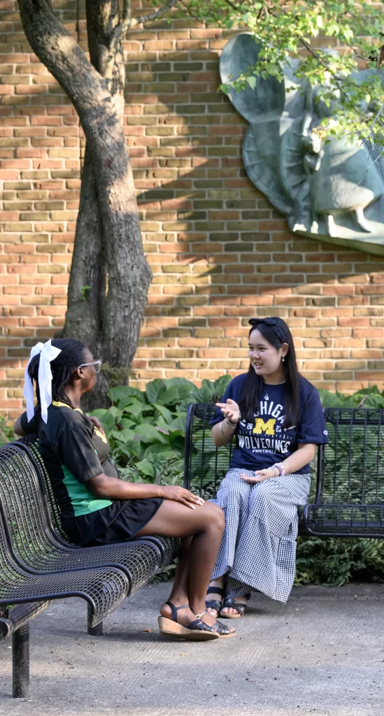 Two women seated on benches in a courtyard, facing each other and talking.