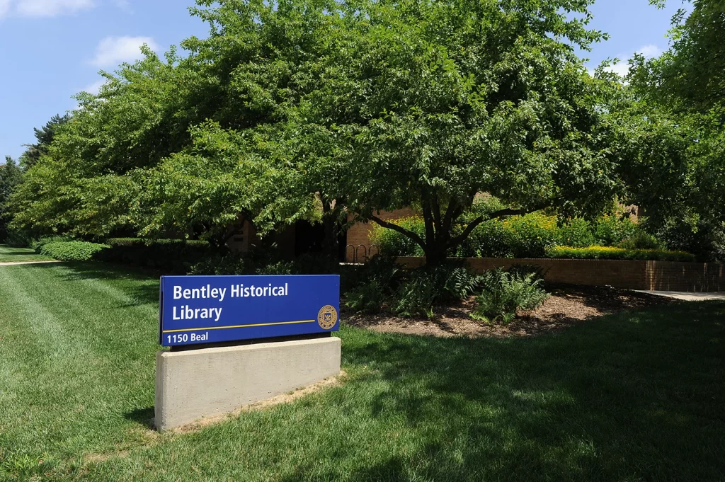 A blue sign with white text says Bentley Historical Library and is surrounded by green grass and trees.