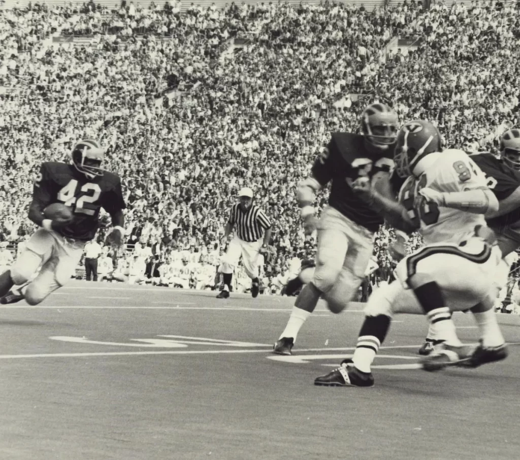 A football player wearing a number 42 jersey carries the ball in a black and white photo taken during a game.