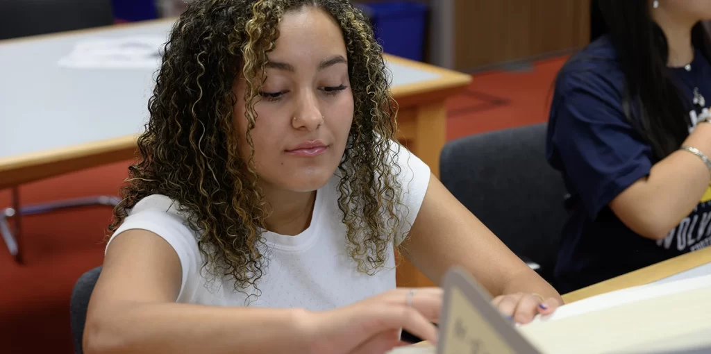 A researcher with curly brown hair in the Bentley Historical Library's reading room peering into an open box full of historical mateirals.