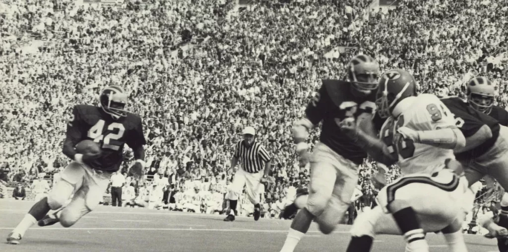 A football player wearing a number 42 jersey carries the ball in a black and white photo taken during a game.