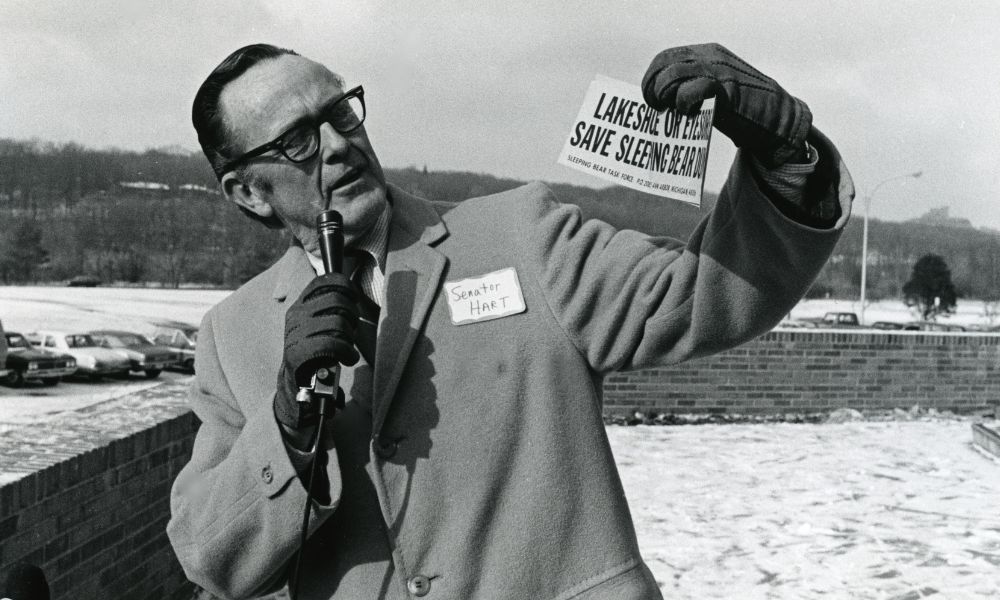 Senator Phil Hart holding a sign that says Lake Shore Or Eyesore Save Sleeping Bear Dunes.