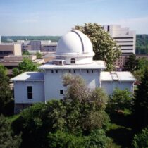 The Detroit Observatory in 1996, pre-restoration, featuring a domed building, trees, and the Ann Arbor skyline.