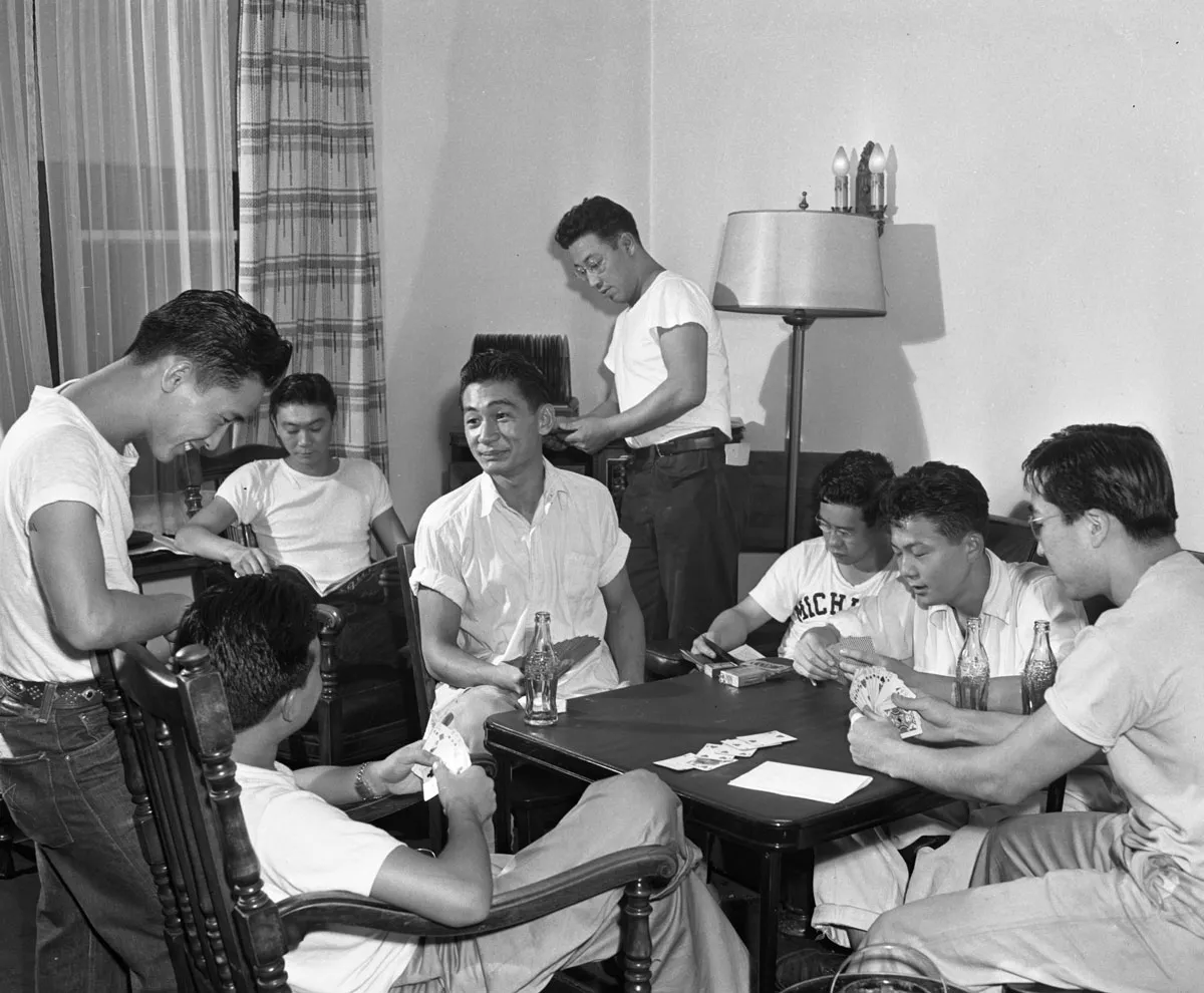 A black and white photo showing several men of Japanese descent gathered around a table playing cards