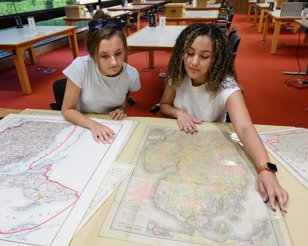 Two women sit at a table in the Bentley's reading room looking at a map of Michigan.