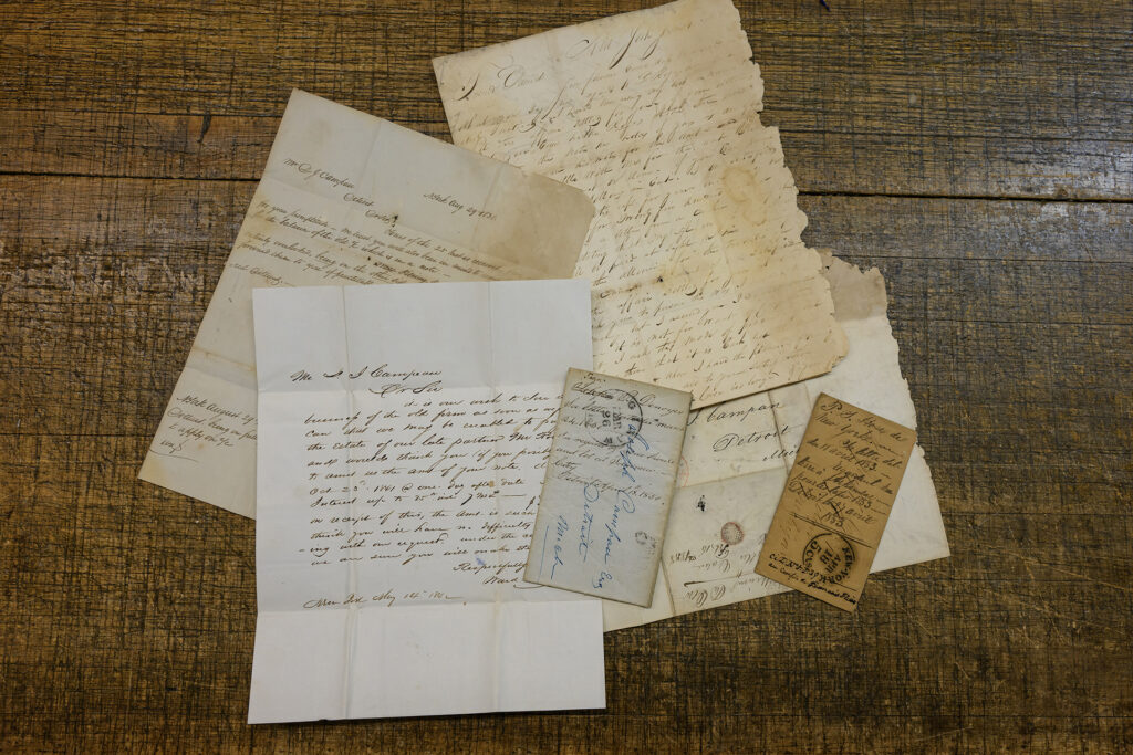 Several old letters and small envelopes arranged on an old wooden desk. The letters have cursive writing that is cramped and hard to read.