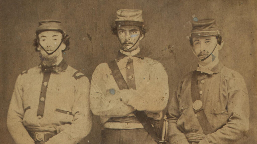 Three men in an old sepia-toned Civil War photo wearing caps with chin straps. Two of the men are holding swords.