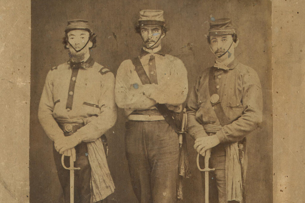 Three men in an old sepia-toned Civil War photo wearing caps with chin straps. Two of the men are holding swords.