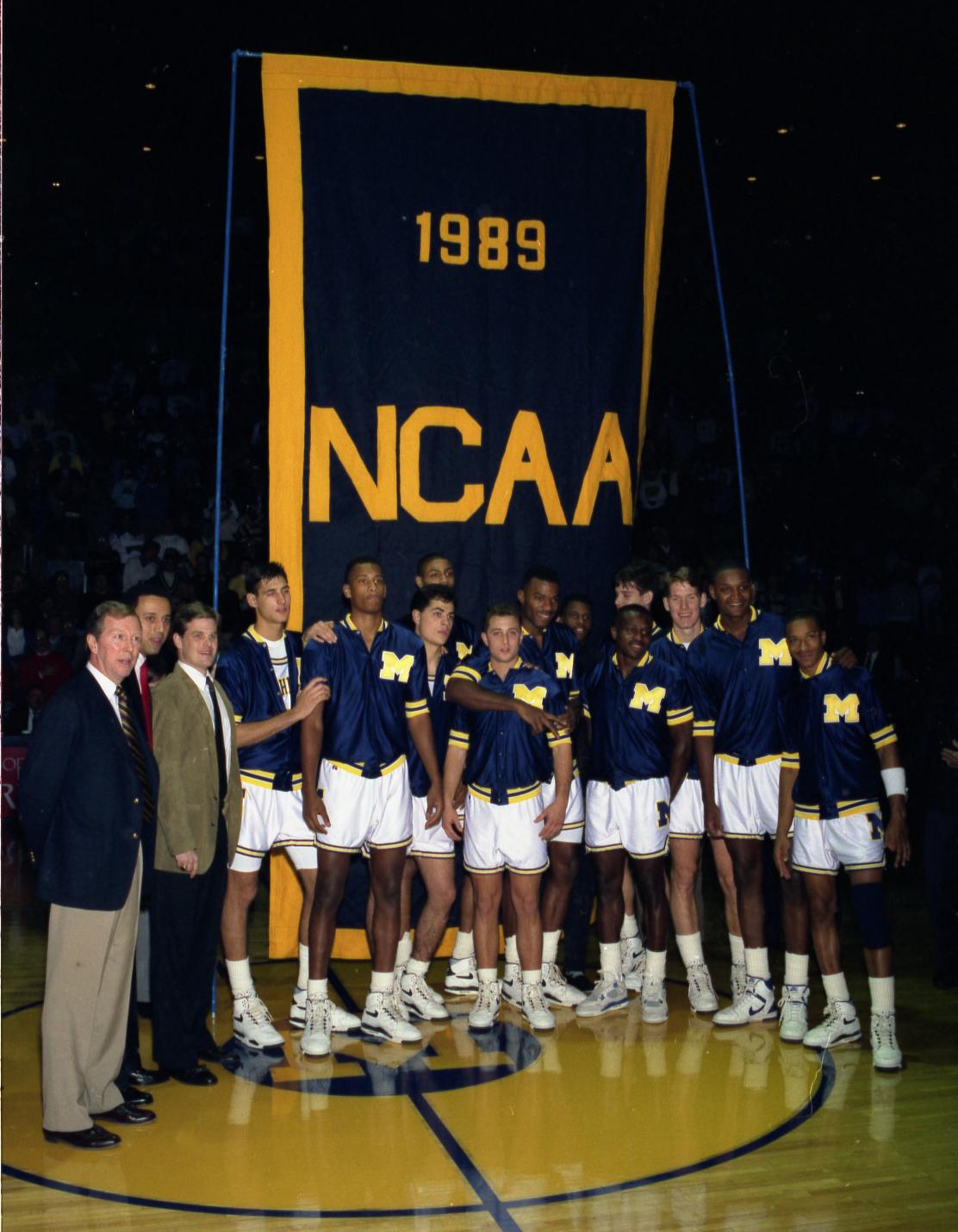 The 1989 U-M Wolverines basketball team stands in front of a navy banner with a maize border and "1989 NCAA" in the center.